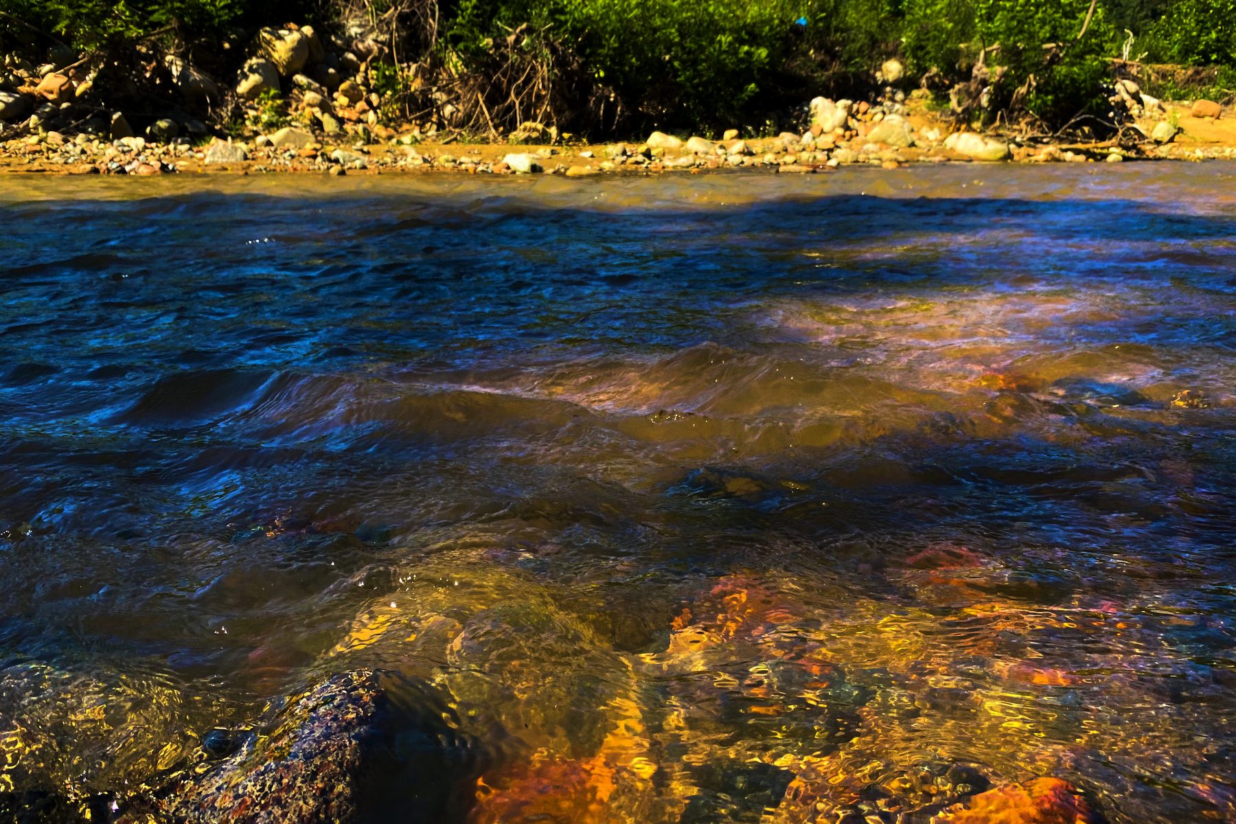 Agua de colores — primer plano del agua de un río corriendo sobre piedras con reflejos de color