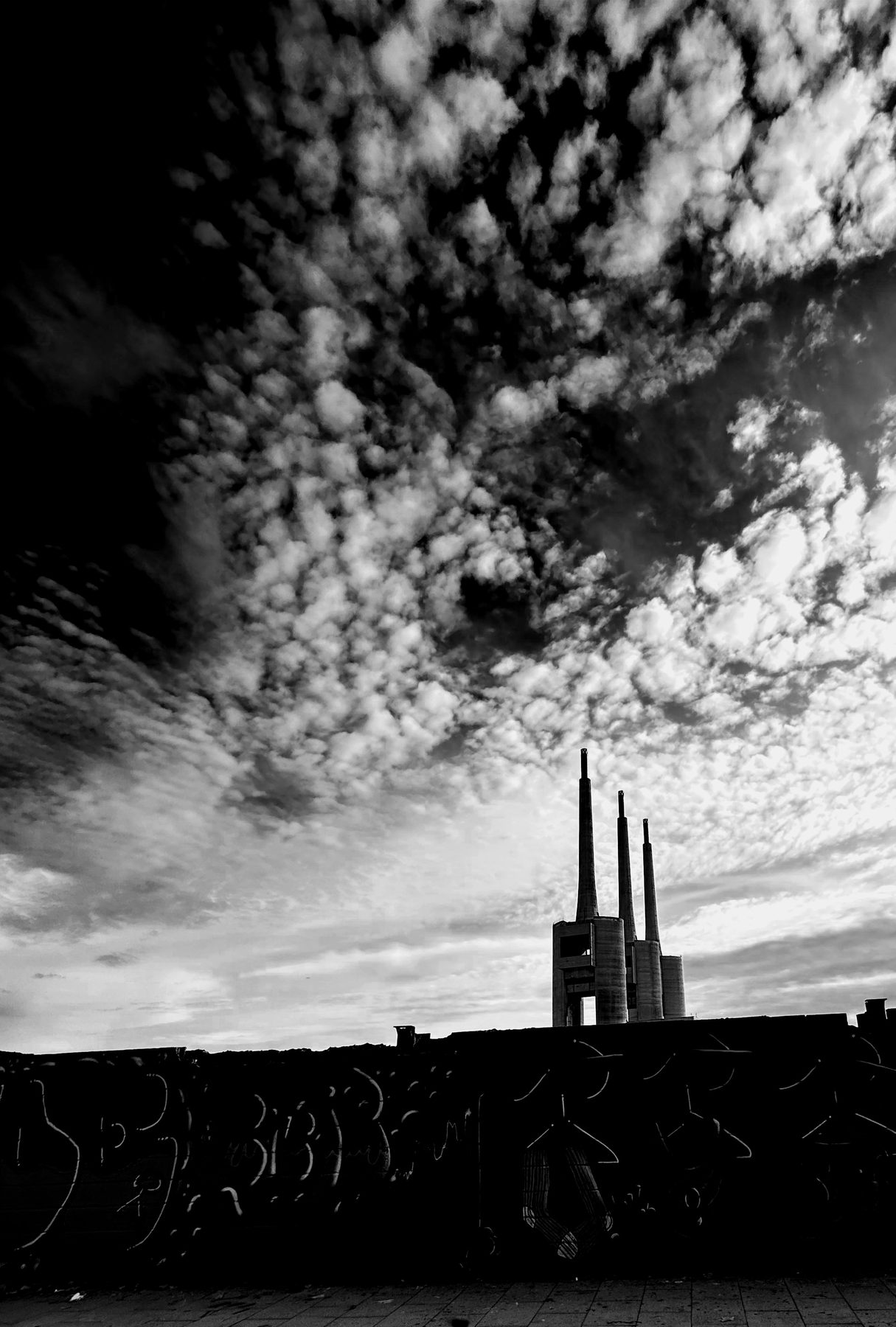 Agujas — Las tres chimeneas de Sant Adrià bajo un cielo de nubes moteadas, en blanco y negro