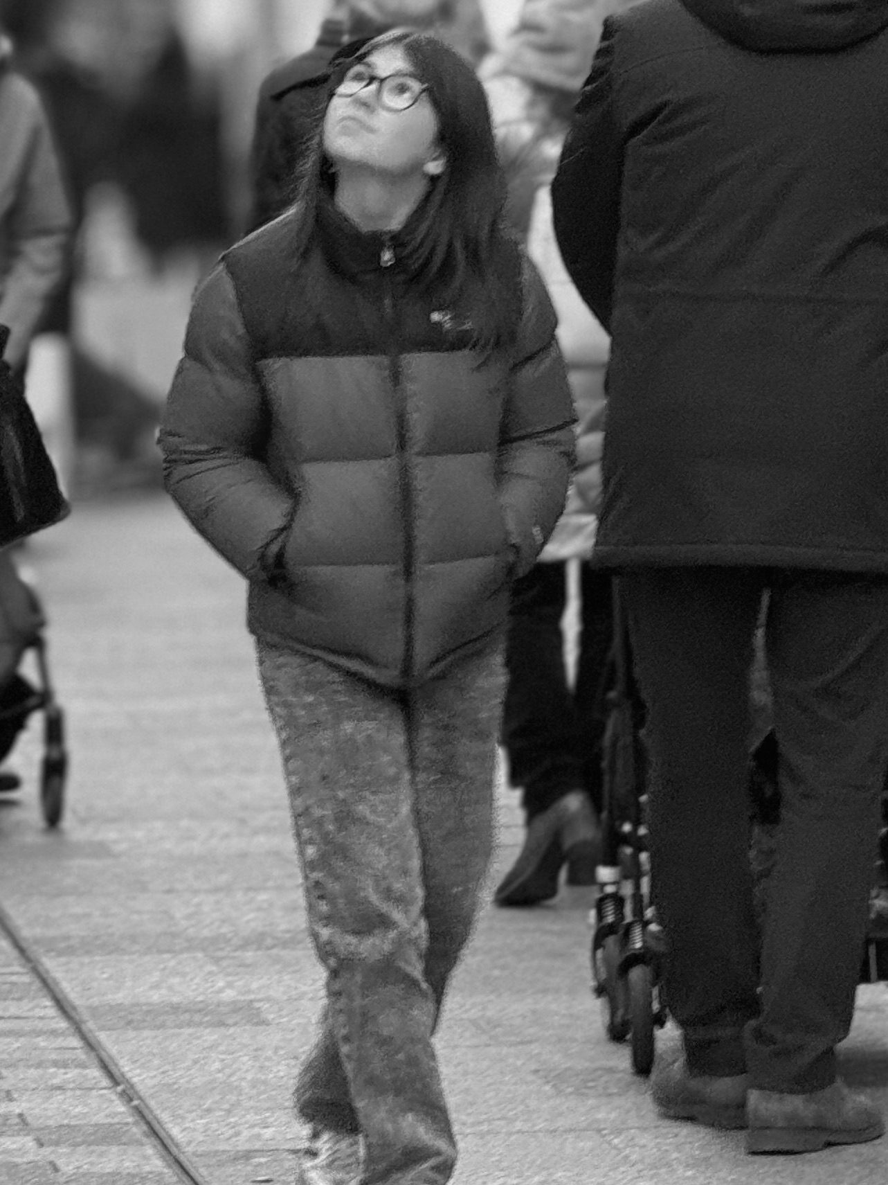 Arriba — mujer con gafas caminando por la calle con la cabeza levantada mirando hacia arriba, en blanco y negro