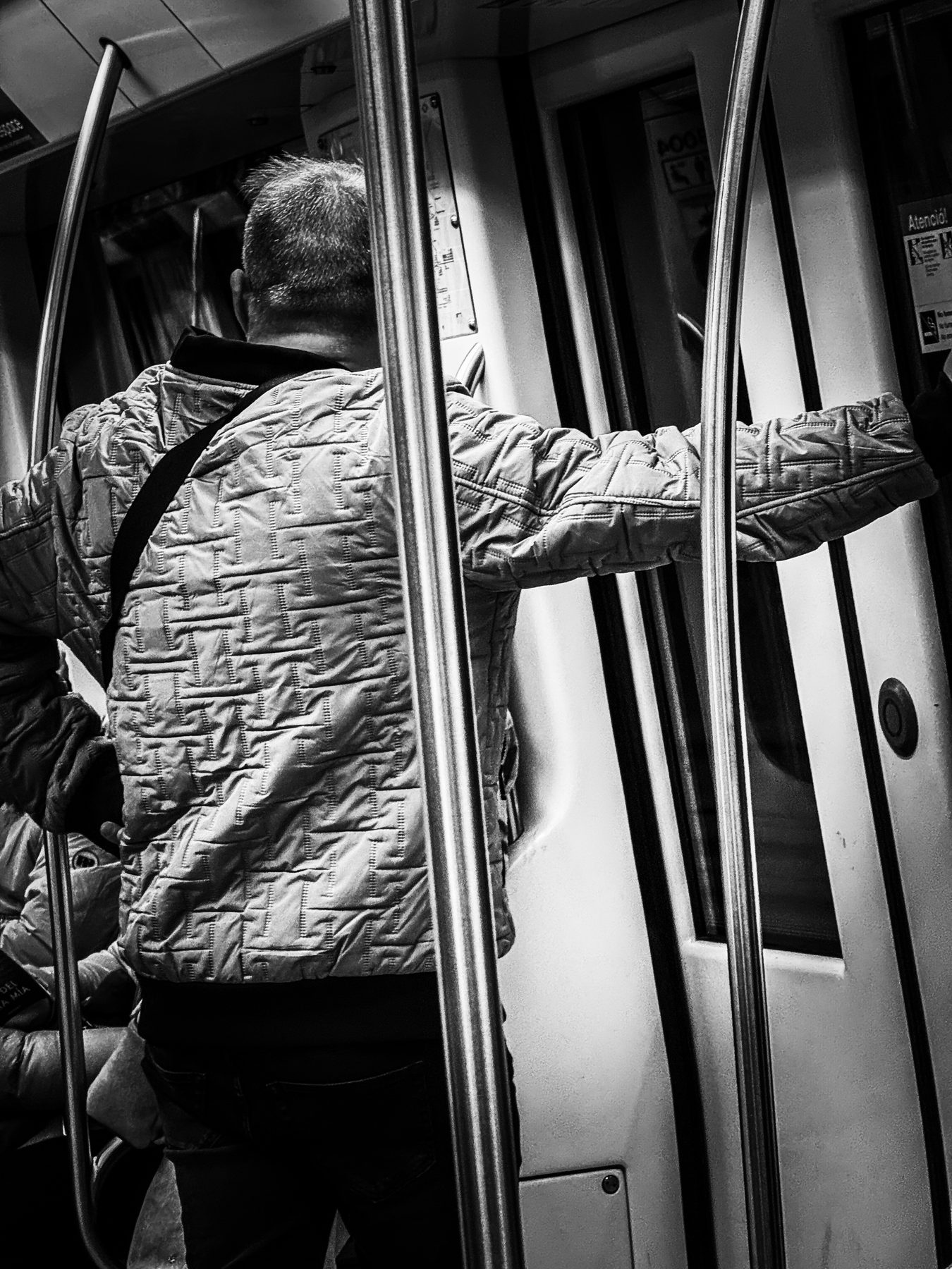 Barras — hombre de espaldas sujeto a las barras de un vagón de metro, en blanco y negro
