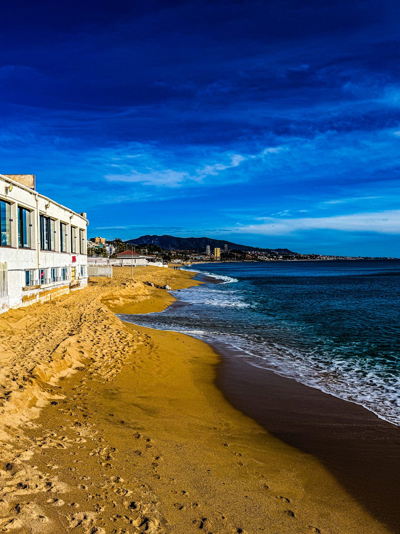 Beso de mar — fachada blanca junto a la playa, arena dorada y mar en un día despejado