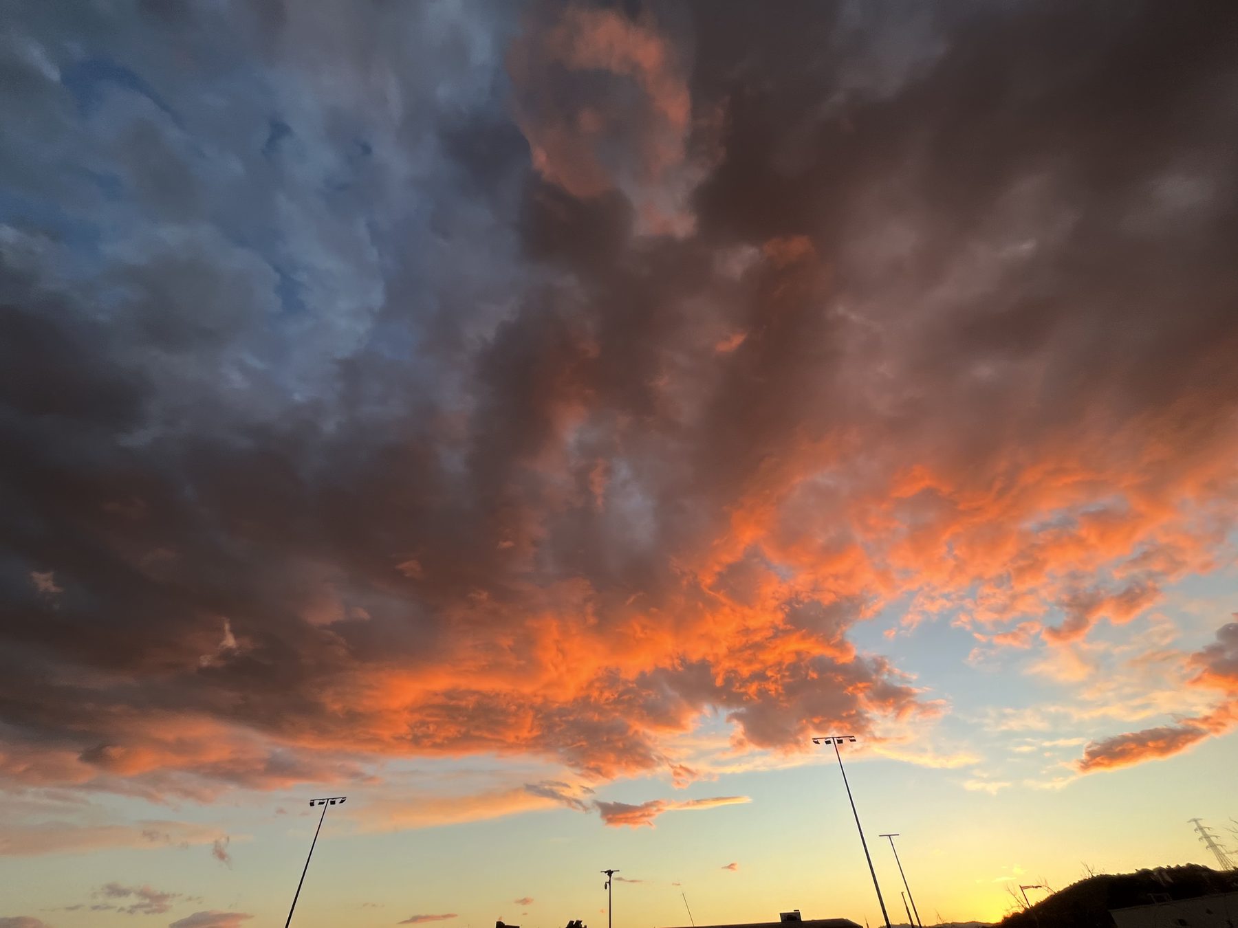 Brasas — Nubes encendidas en naranja sobre el perfil de un pueblo al anochecer