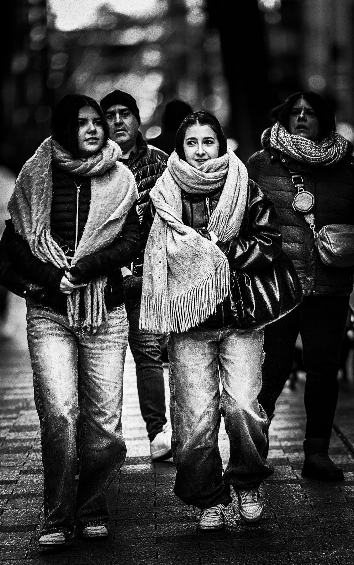 El frío las junta — dos chicas con bufandas grandes caminando del brazo por una calle en invierno, en blanco y negro