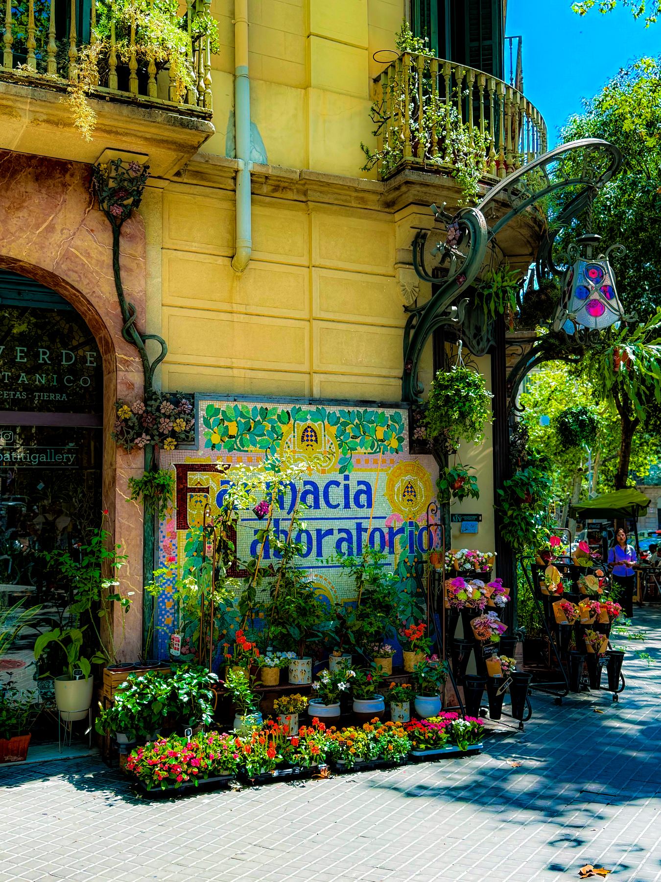 Farmacia — mosaico modernista de una antigua farmacia, comido por las plantas de una floristería, con farola de forja y cielo azul