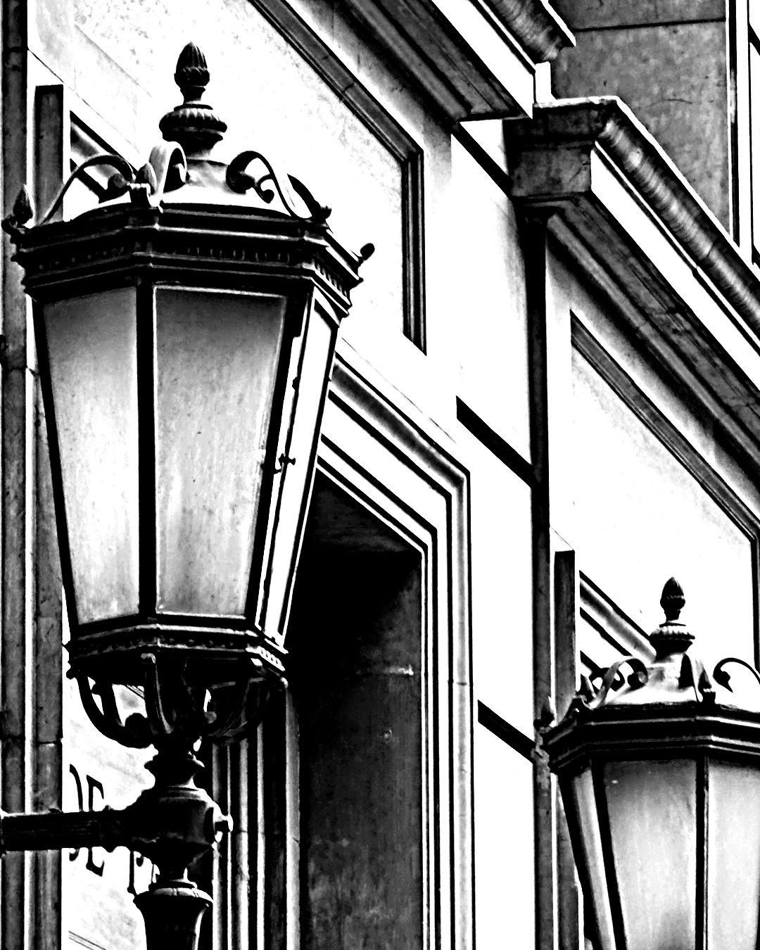 El mismo hierro — dos faroles de hierro sobre la fachada de piedra de un edificio, en blanco y negro de alto contraste