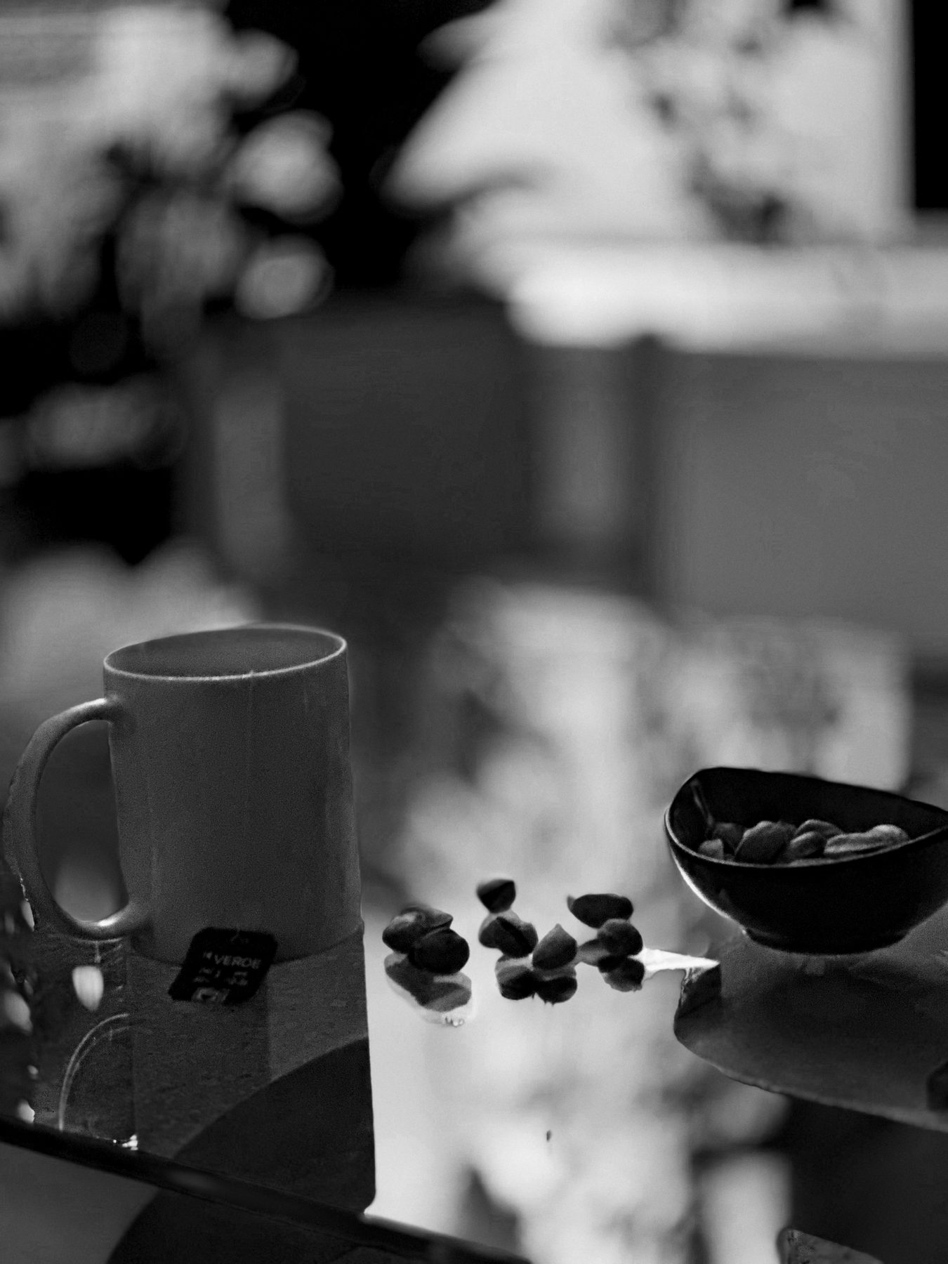La pausa — taza de té con la etiqueta colgando junto a un cuenco de frutos secos sobre una mesa de cristal, en blanco y negro