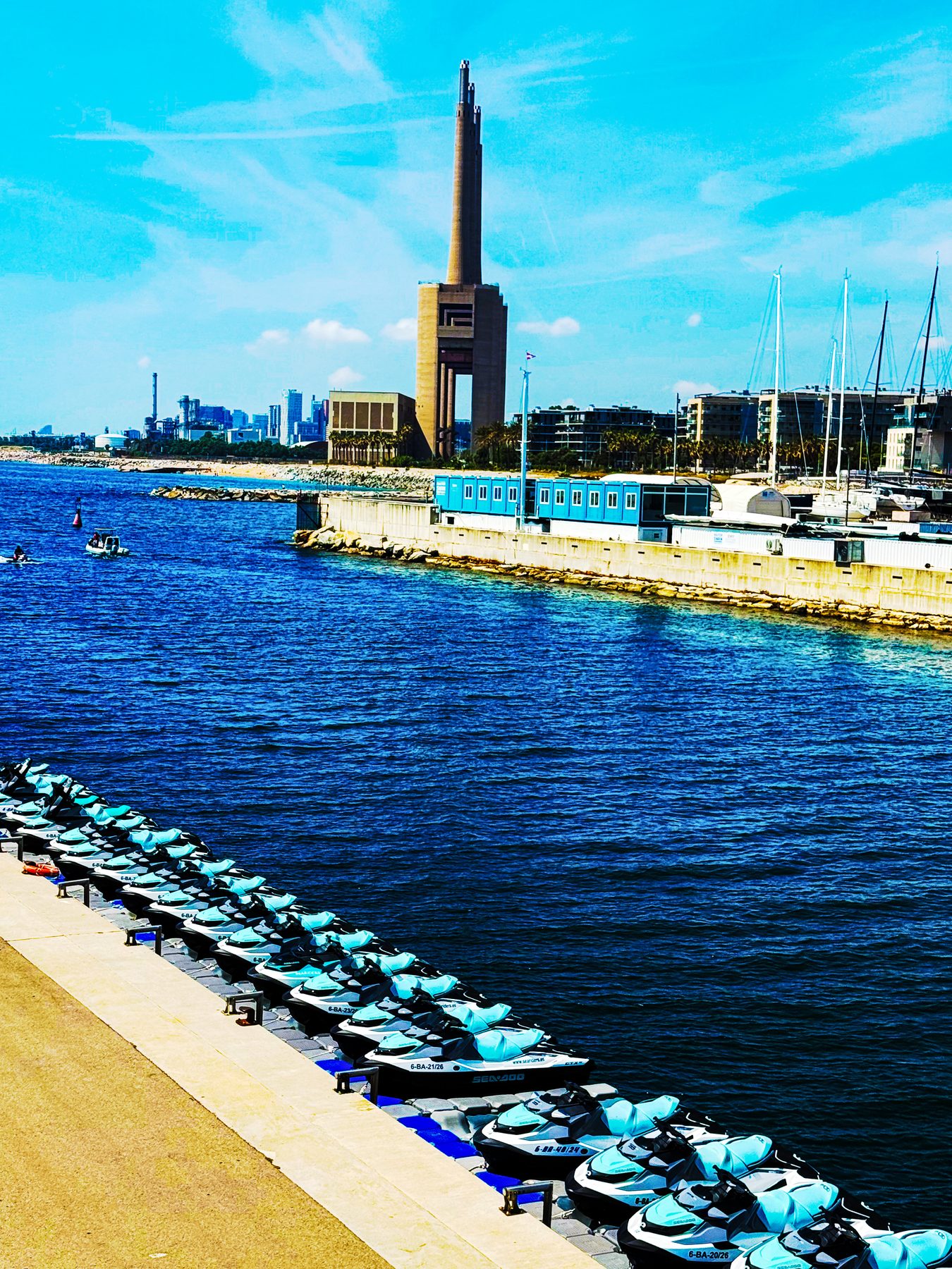 Motos de agua — motos acuáticas alineadas junto al puerto, con una chimenea industrial al fondo