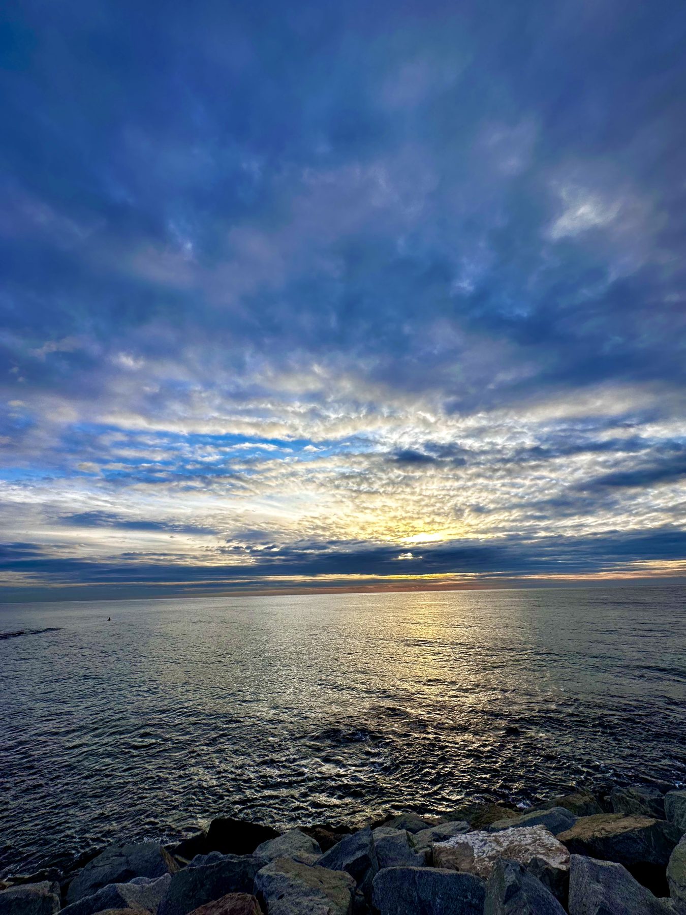 Se va por donde vino — Rocas de espigón, mar y el reflejo del sol bajo un cielo azul