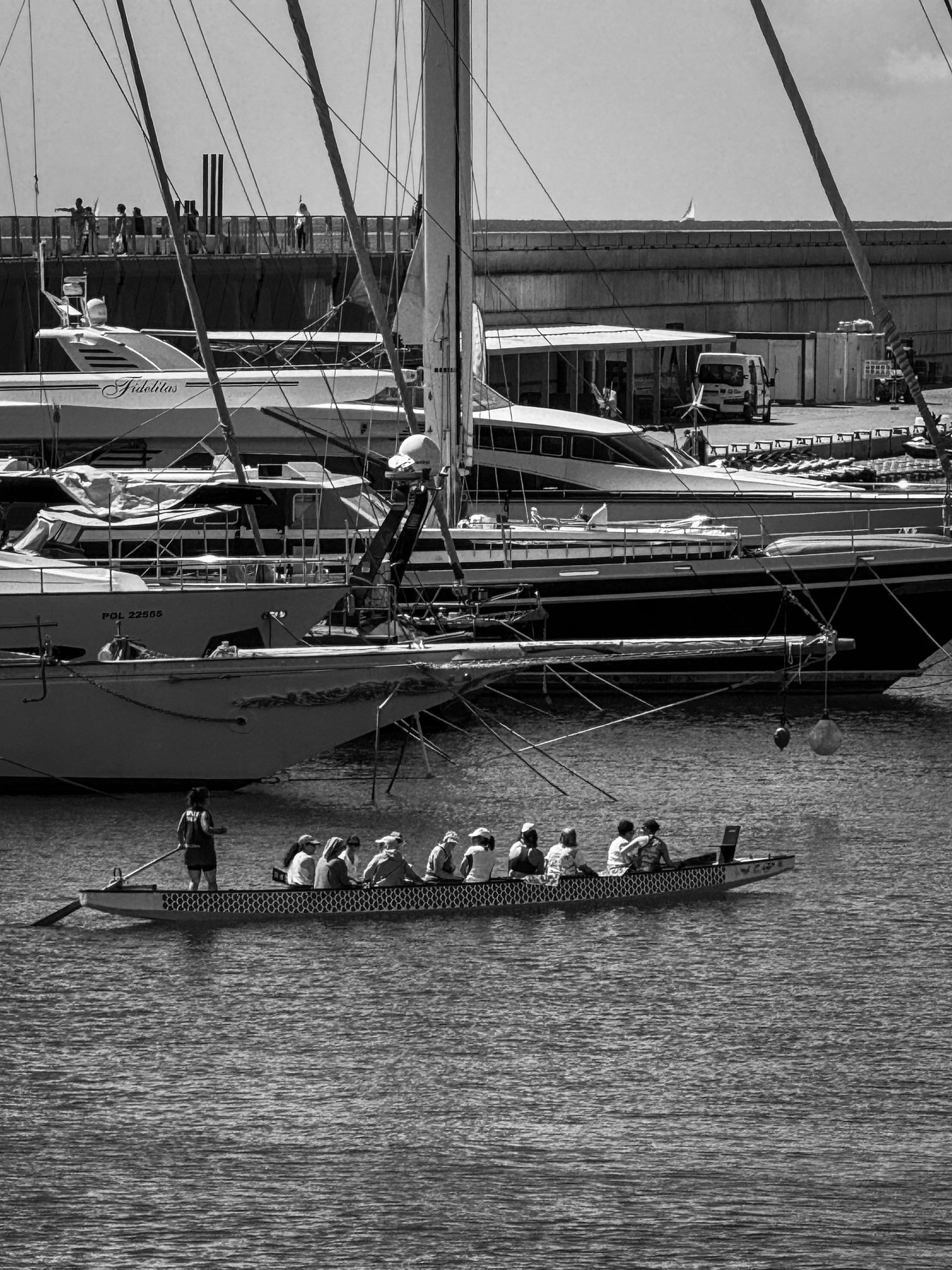 Todos a una — equipo de piragüismo remando entre yates amarrados en el puerto