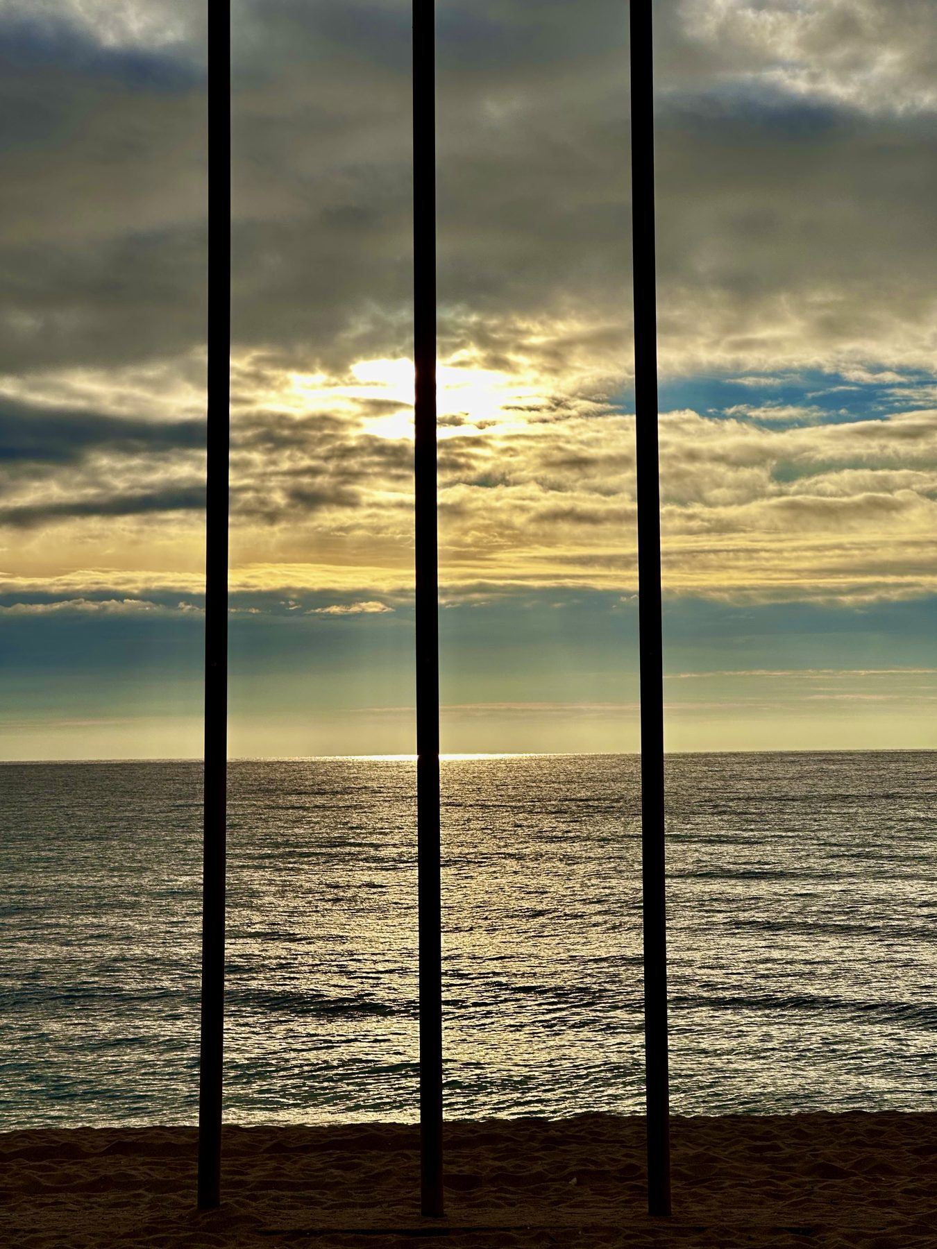 Tres postes — Tres postes verticales recortados contra el mar y el cielo del atardecer